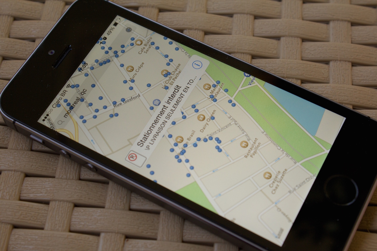 Mobile phone over a table. Its screen shows a map with streets and blue dots denotating parking spots.